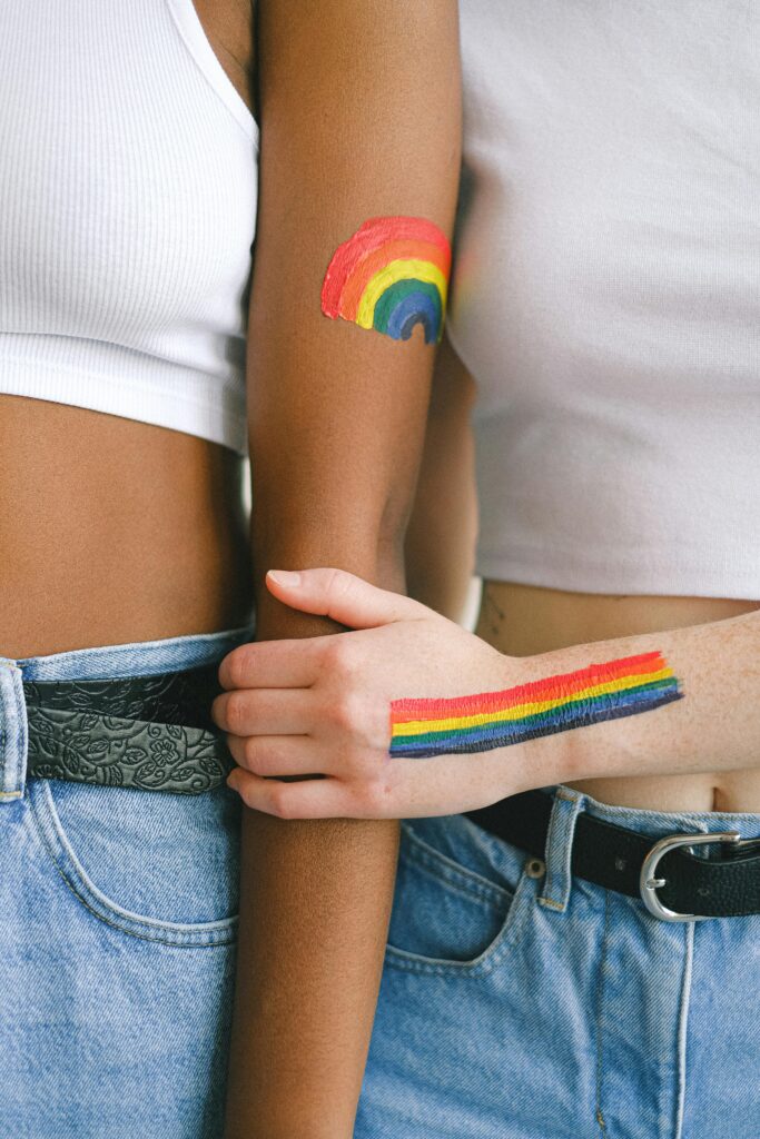 Close-up of an interracial couple showing LGBTQ pride with rainbow body paint on their arms.